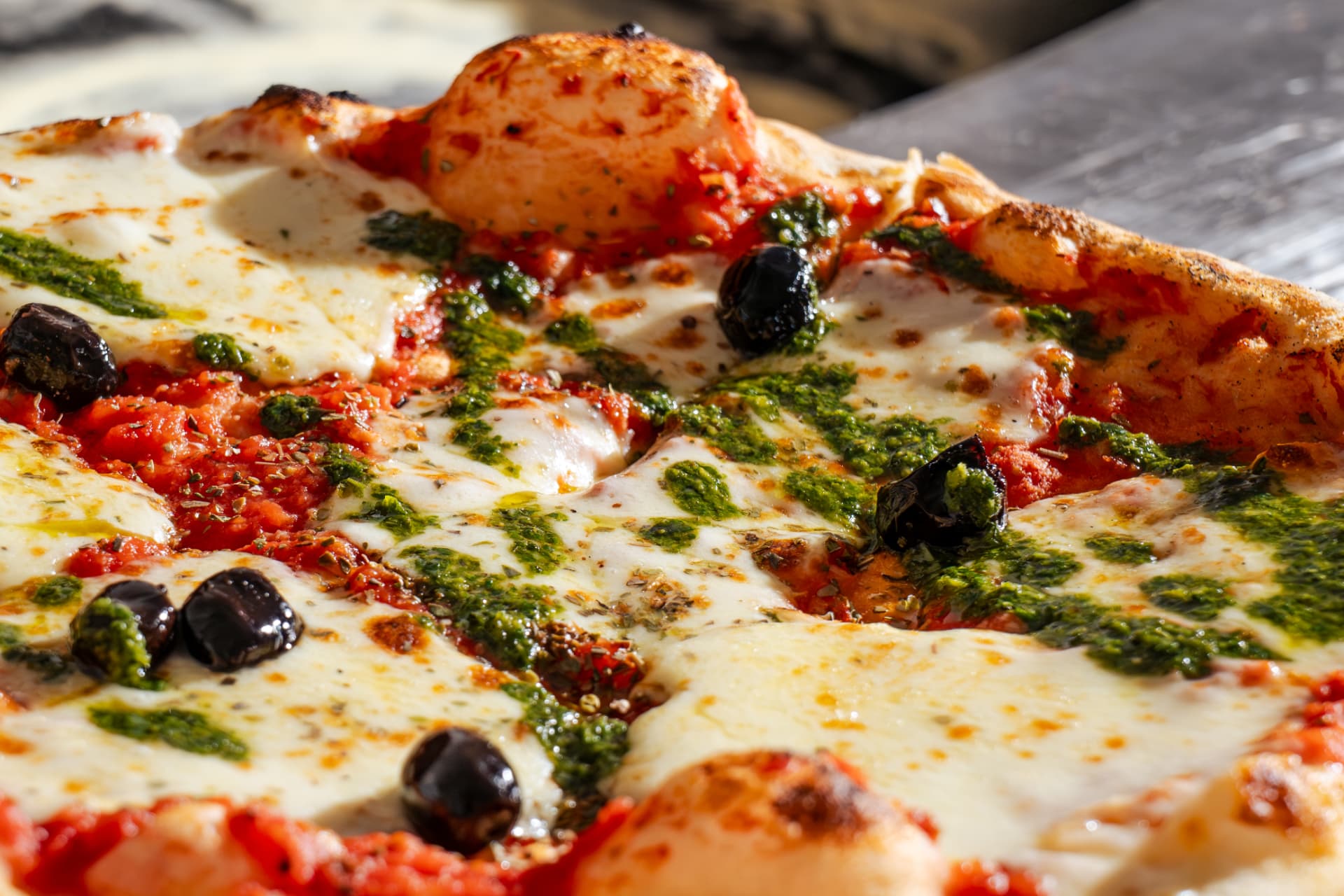 Gros plan sur une pizza au feu de bois, mozzarella fondante et pistou
