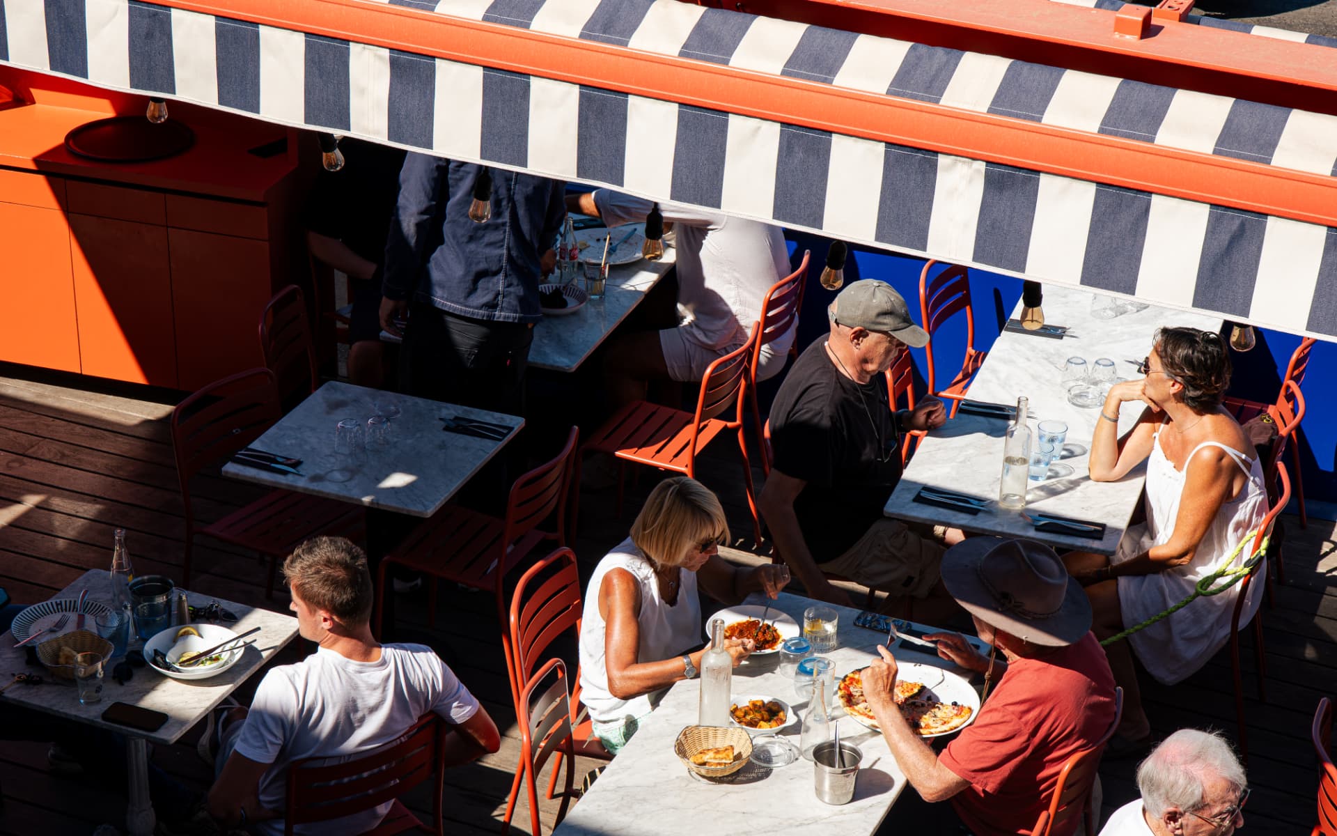 Terrasse animée du Lou Mar sous les stores rayés bleu et blanc